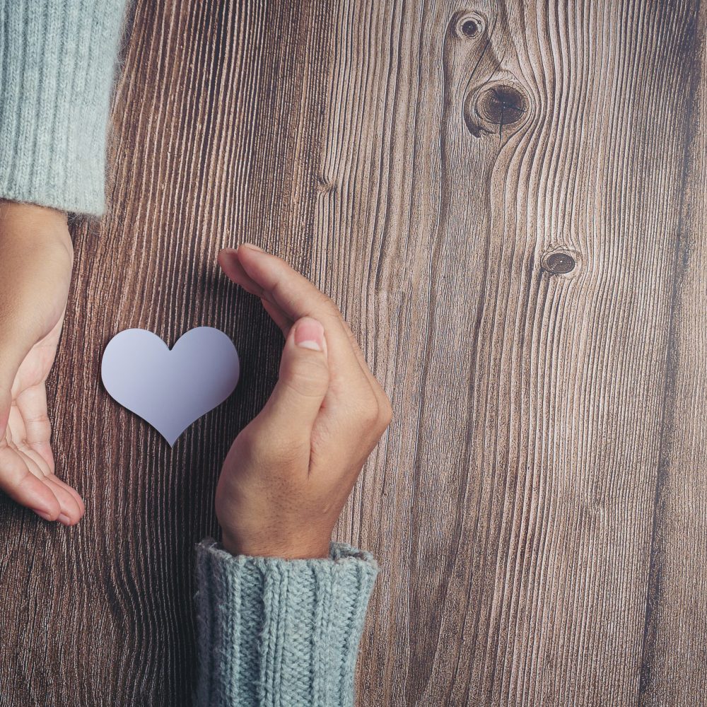 paper heart and couple's hands on wooden table